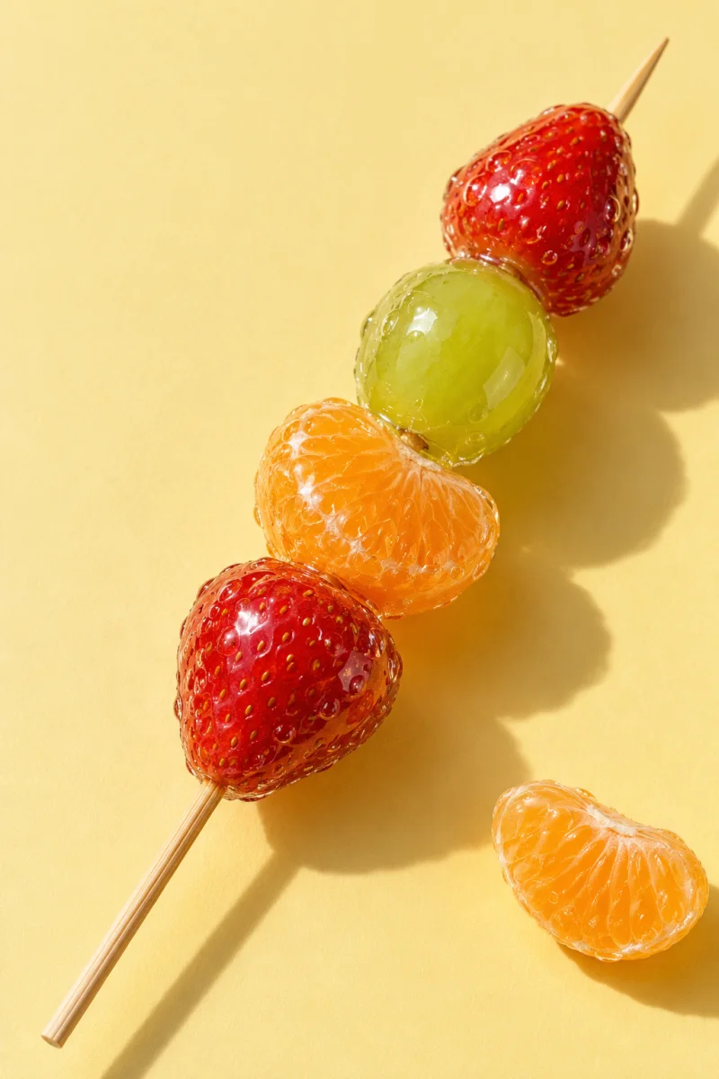 Strawberry, grape and mandarin tanghulu on a warm yellow background